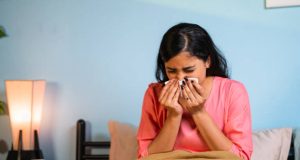 Young girl suffering from cold by sneezing at home while sleeping on bed - concept of healthcare, infection and unhealthy