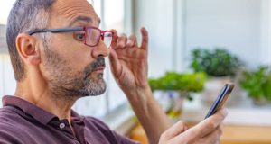 Spain. Adult man with beard putting on presbyopic glasses to see closely the mobile phone screen