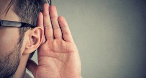 man holds his hand near ear and listens carefully isolated on gray wall background