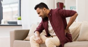 people, health care and problem concept - unhappy man suffering from pain in back or reins at home